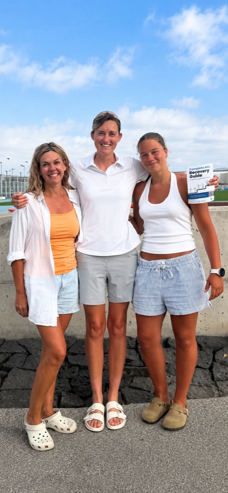 Three smiling women outdoors holding the Complete ACL Recovery Guide