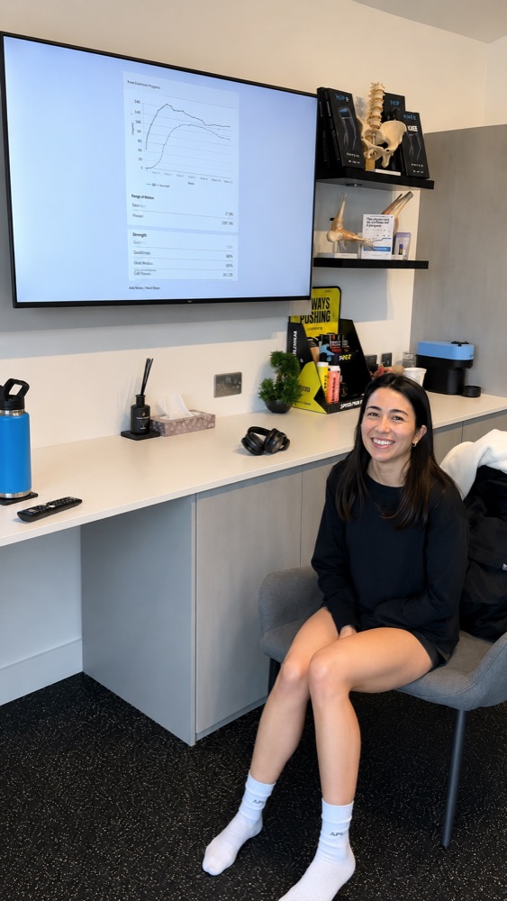 Smiling patient beside her knee extension progress charts